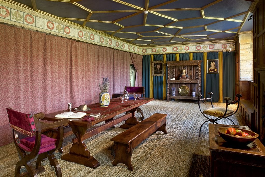 an old fashioned smart interior with tapestries on the wall and a long wooden table with wooden benches and a wooden cabinet