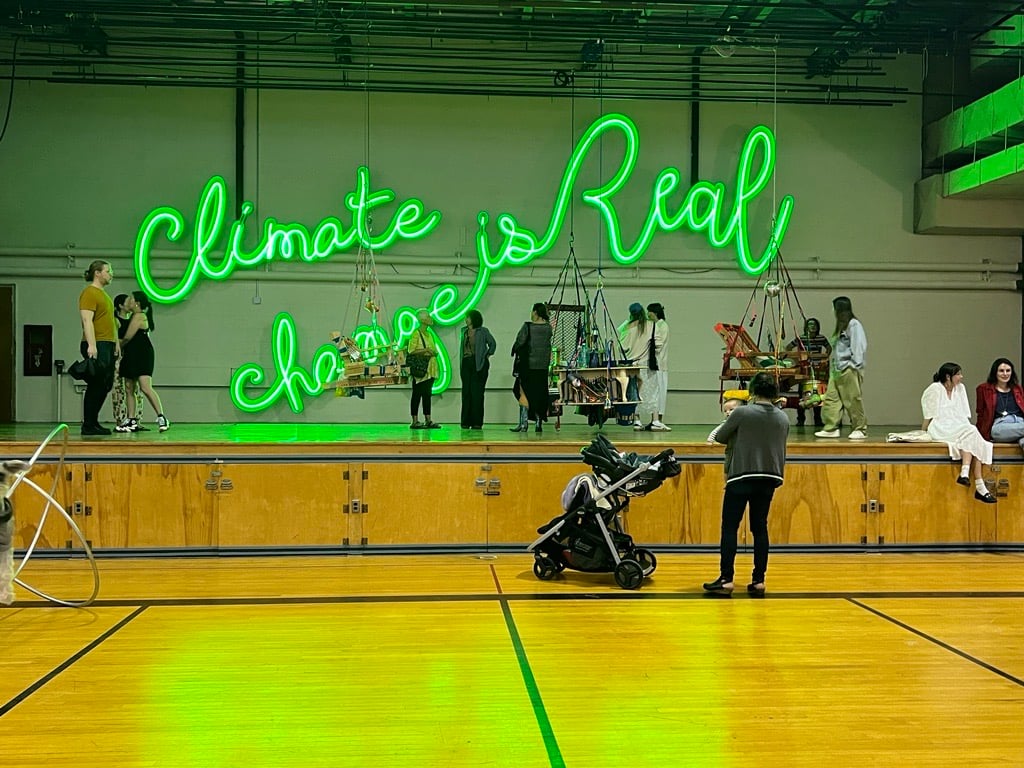 A green neon sign reading "climate change is real" in the gym on The Campus