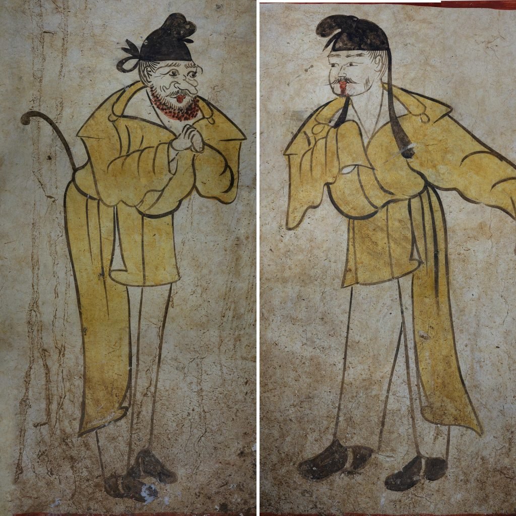 two asian figures dressed in yellow robes stand sentry on the corridors of the tomb