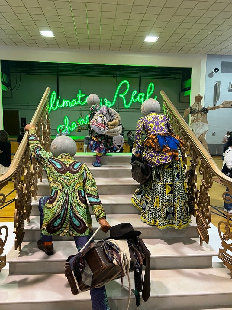 figures in 19th century clothes done with African fabrics, with travel bags, going up an ornate staircase