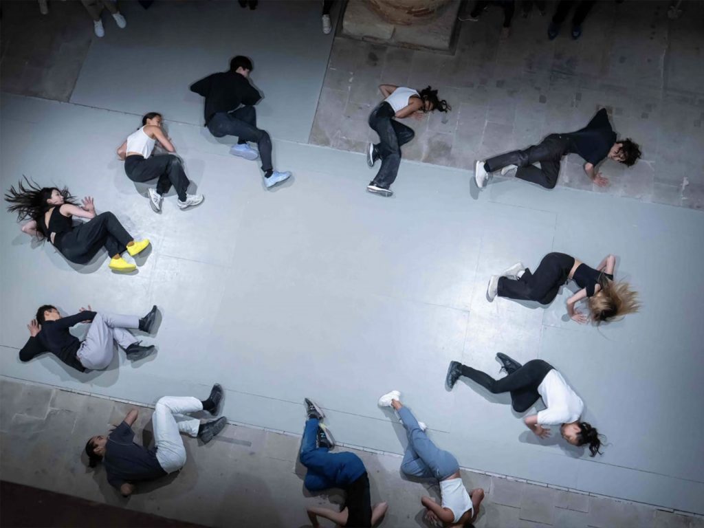 This photo depicts a group of performers lying on the floor in circle