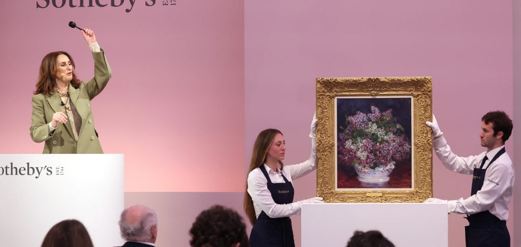 an image of Helena Newman holding the gavel with two handlers holding a Renoir paitning