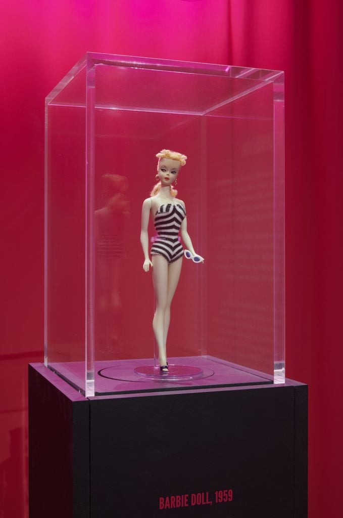 a display case features a vintage barbie doll wearing a striped swimsui, against a pink background