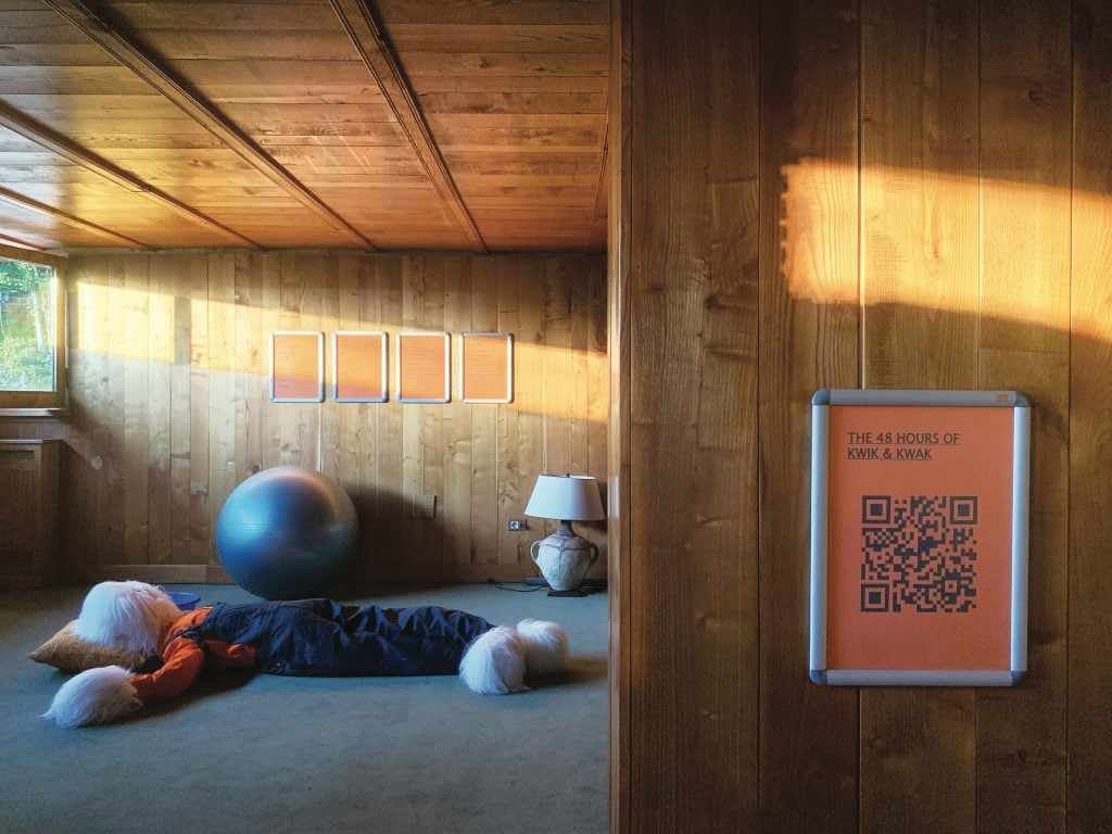 installation in a wood panelled room that includes a large puppet lying on the floor