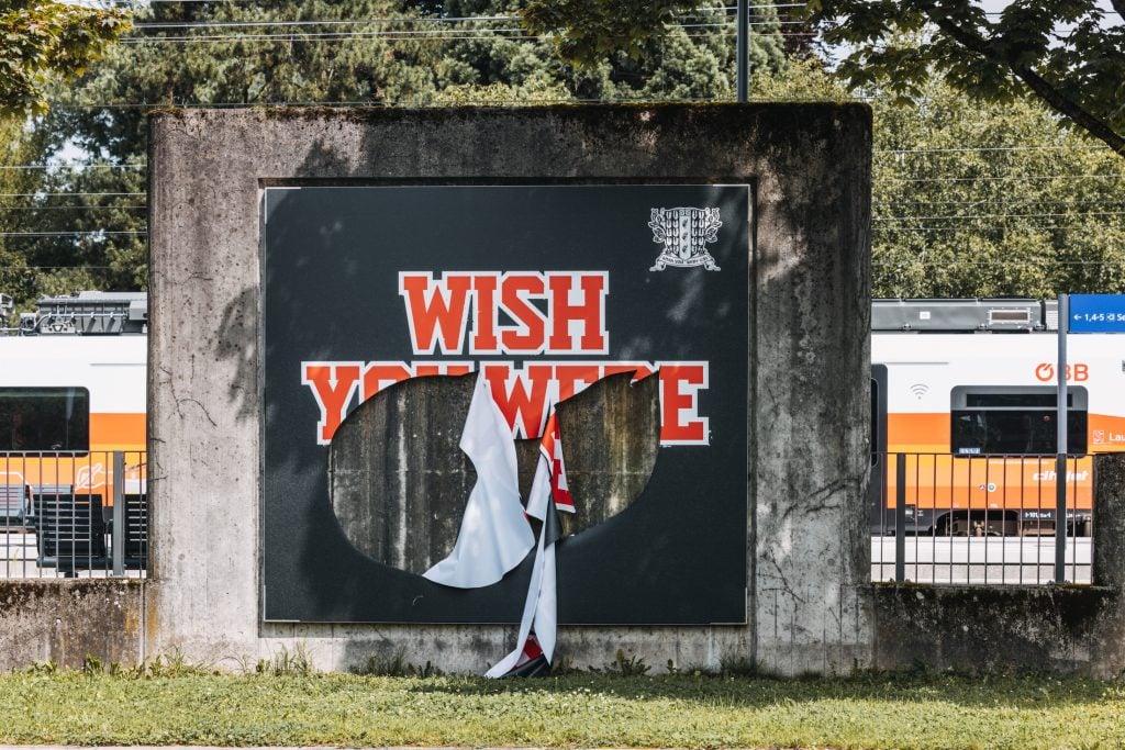 a large poster on a slab of stone in a public place is visibly slashed in a violent way but you can make out the word 'wish' in red font