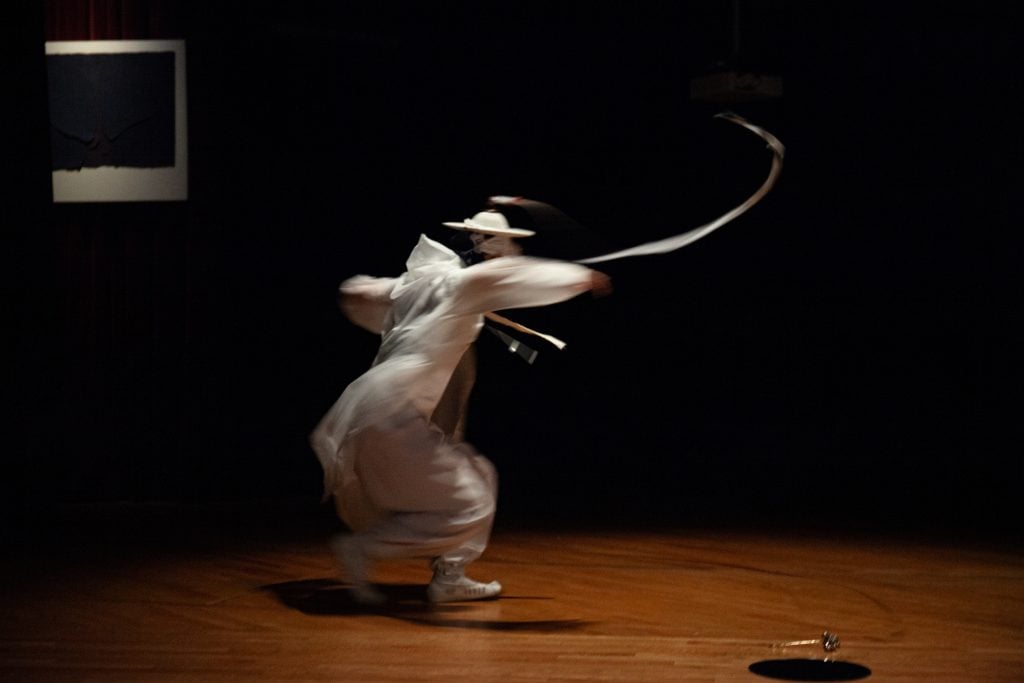A performer dressed in white outfit and a white hat holding a whip in swirling movement
