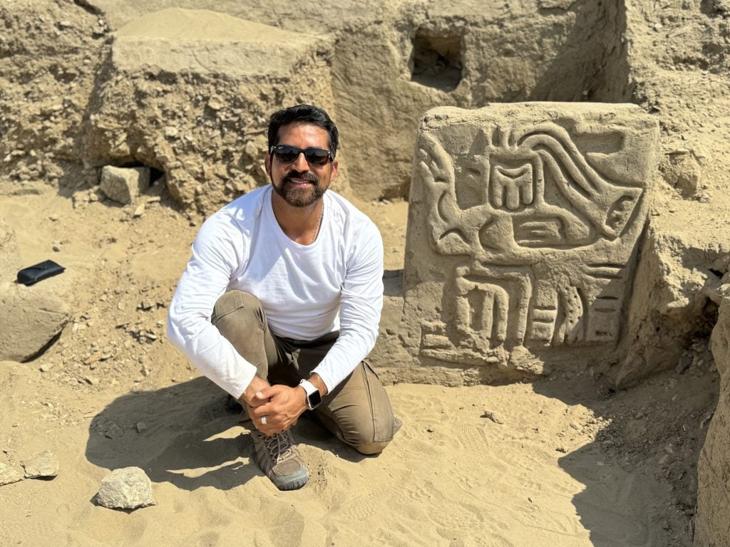 a man stands in front of a highly detailed block of stone discovered in peru