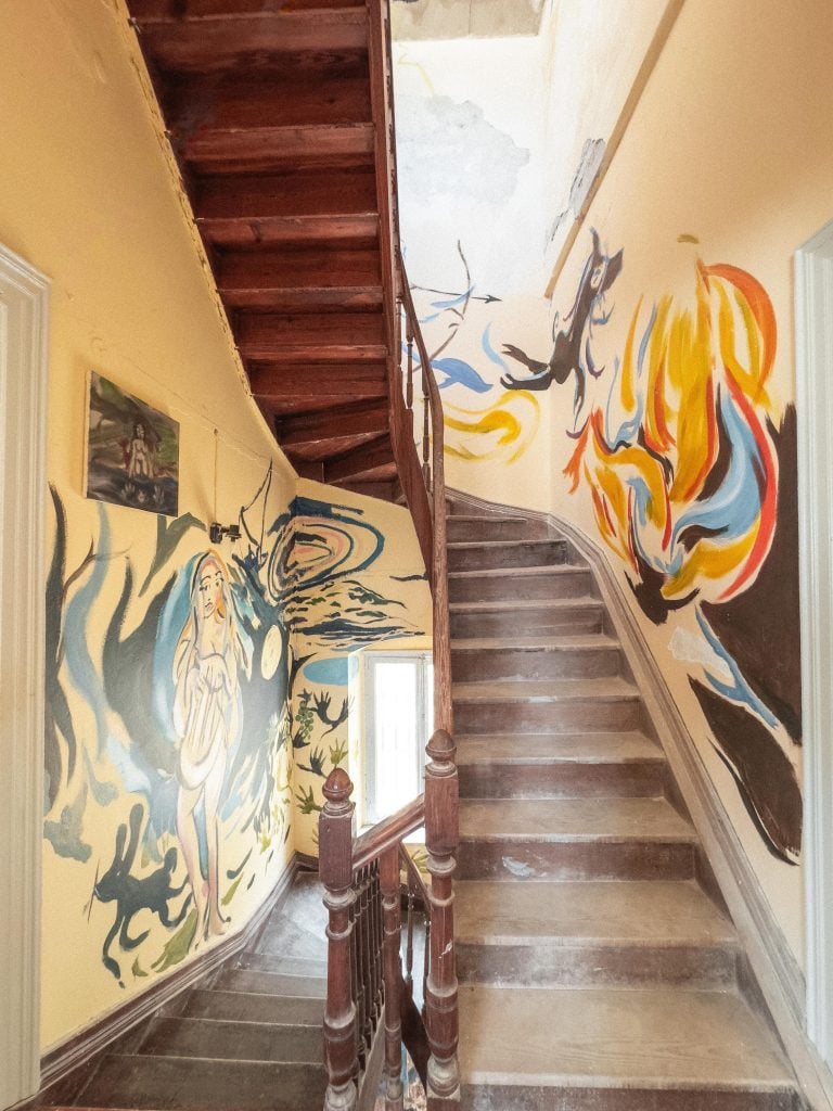 a wooden staircase lined with walls that are covered in a painted mural that is coloruful and have some figures and faces in it but is otherwise quite abstract