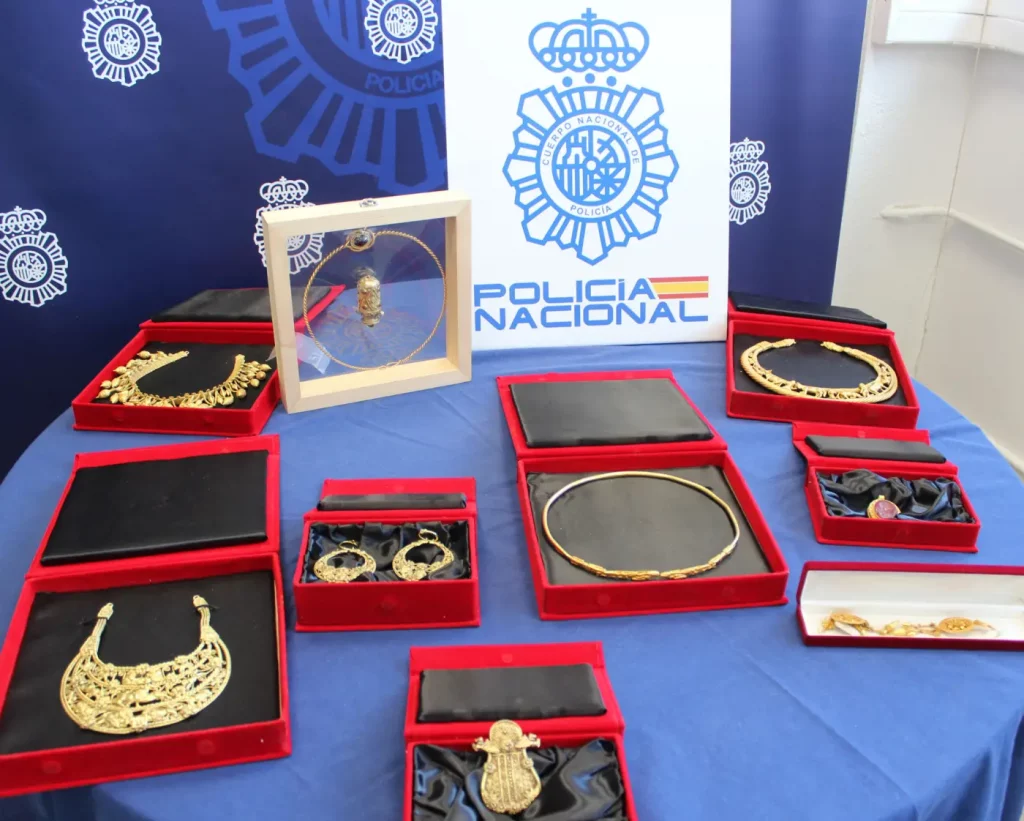 an array of gold jewellery in open red boxes on a table with the Spanish police logo on a sign behind