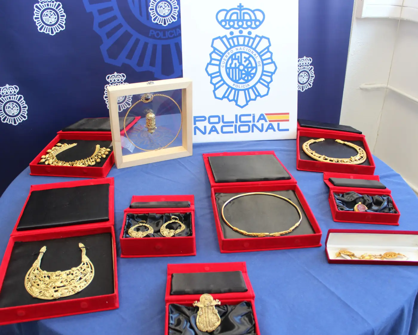 an array of gold jewellery in open red boxes on a table with the Spanish police logo on a sign behind