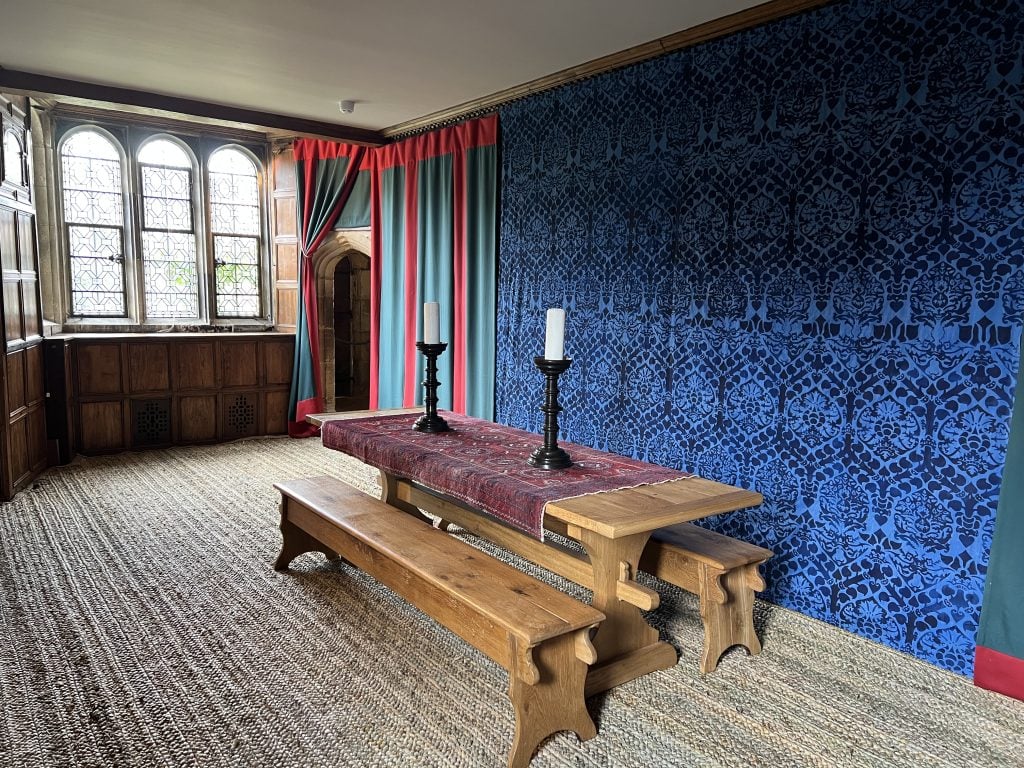 an old fashioned interior with a blue tapestry covering one wall and a humble wooden table with wooden benches