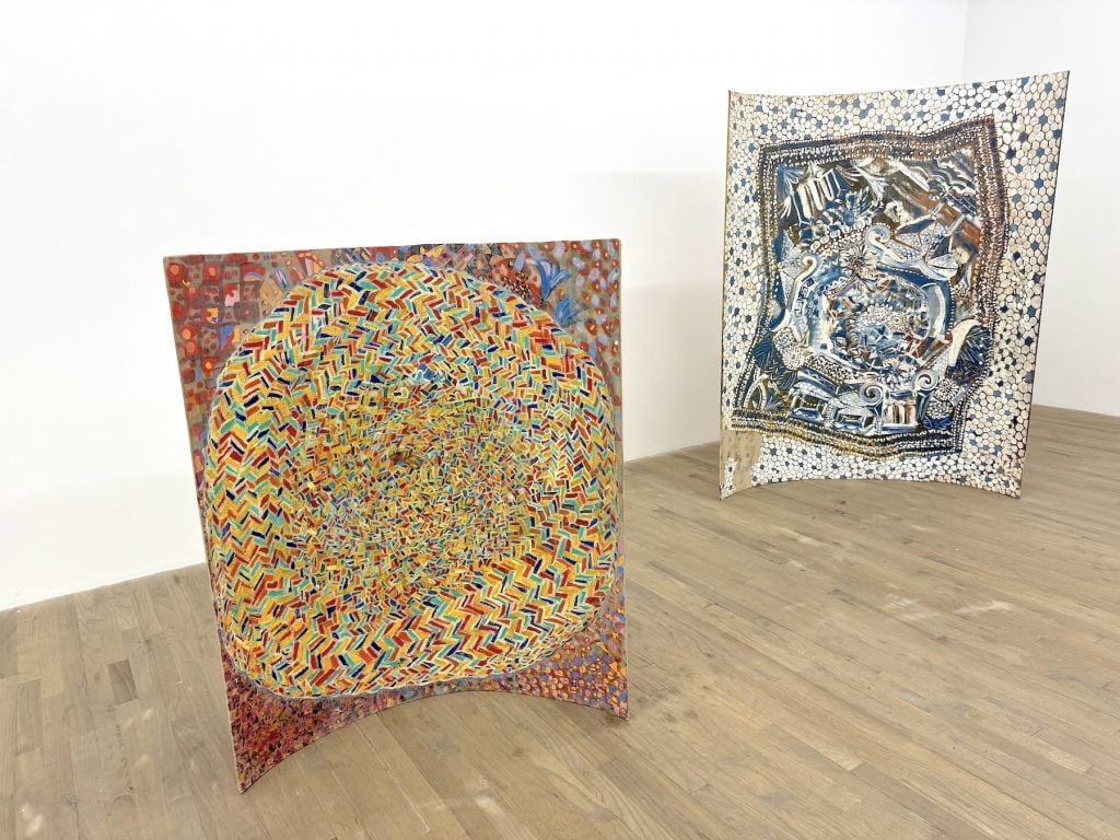 Two abstract works of art stood up on the floor of a gallery