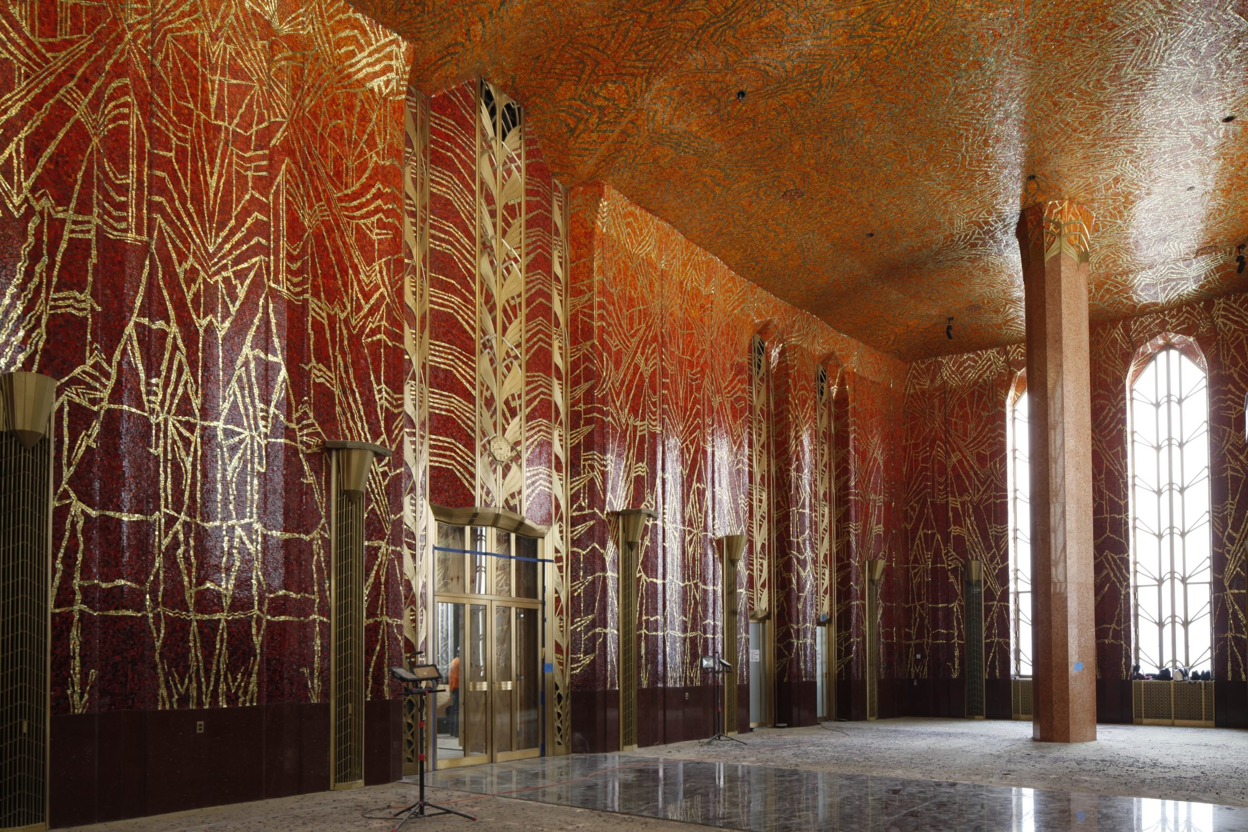 A high-ceilinged room with ornate Art Deco mosaics by Hildreth Meière fading from blood red to bright orange on the ceiling, decorated with sparkling gold designs.