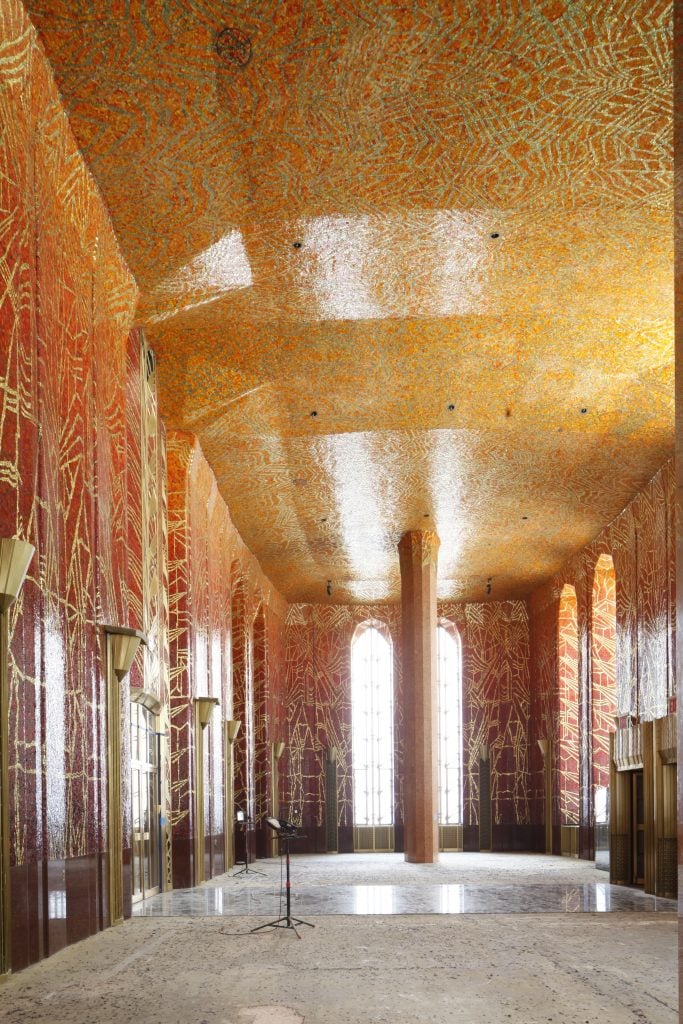 A high-ceilinged room with ornate Art Deco mosaics by Hildreth Meière fading from blood red to bright orange on the ceiling, decorated with sparkling gold designs.