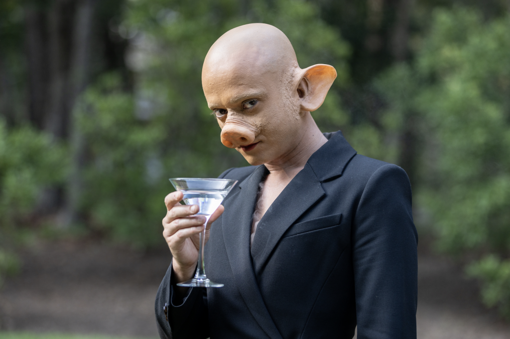 A performance artist in a pig mask sips a martini. 