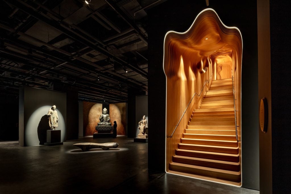 A mysterious staircase leading to an exhibition space, with Buddhist statues on show in the dark.
