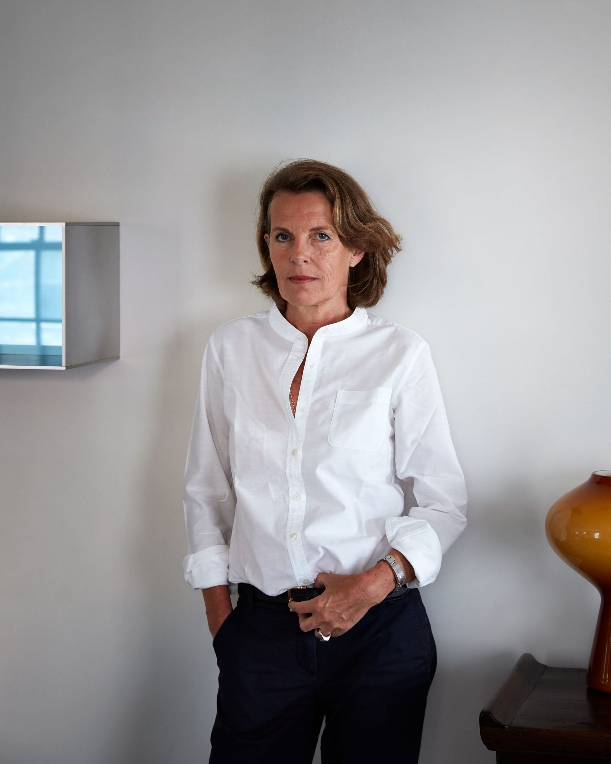 A white woman in a white shirt stands in front of a wall