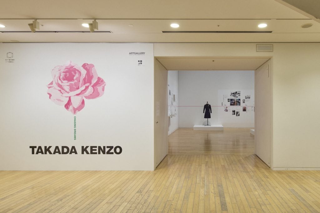 an entrance to a museum exhibition of Takada Kenzo shows a drawing of a pink flower on a white wall
