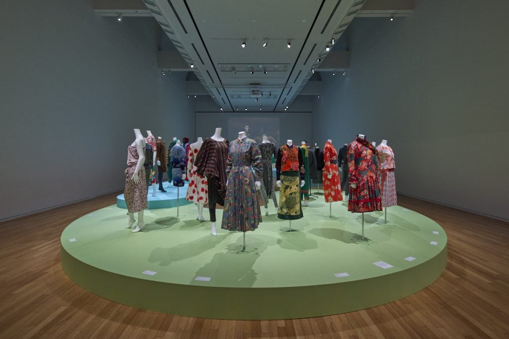mannequins wearing kenzo dresses are displayed on a large green platform in a museum gallery 