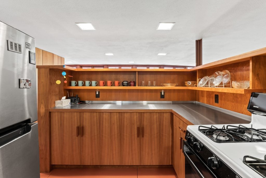 A modernist kitchen featuring wood panelling, stainless steel counter and colourful pots. designed by frank lloyd wright