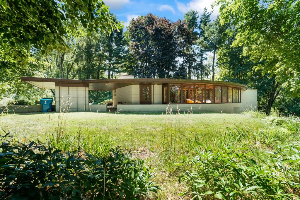 a modernist house with large windows in a lush green garden. designed by Frank Lloyd Wright