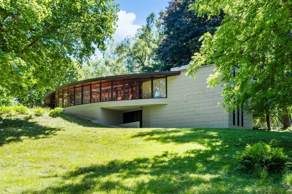 一栋现代化的房子，有大窗户，坐落在郁郁葱葱的绿色花园中。由弗兰克·劳埃德·赖特设计