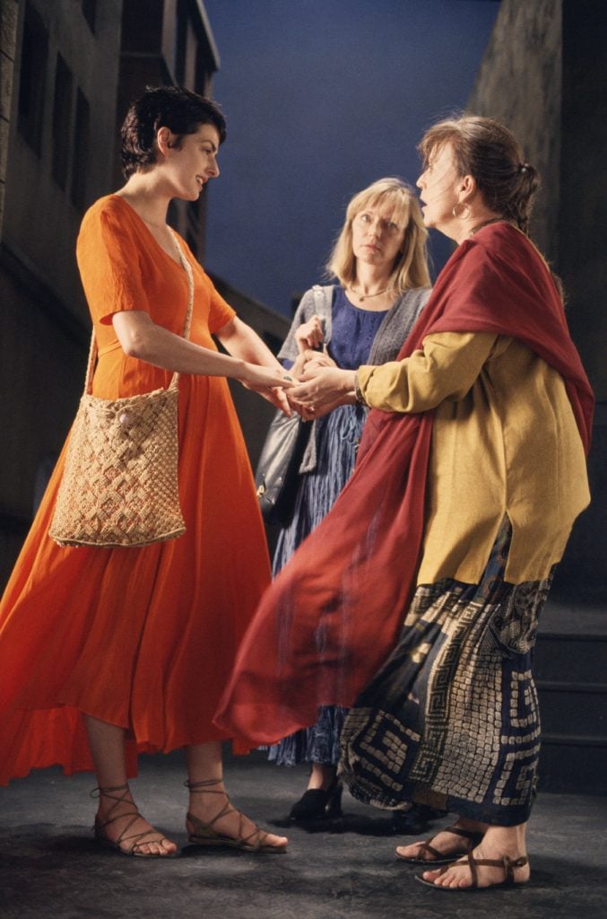 three women facing in to each other in an intimate gathering, they were ancient style clothes in bright colours like orange