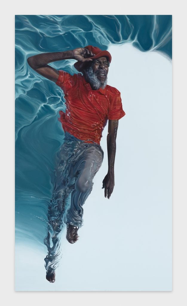 a black man in a red tshirt is seen lying on his back in a pool of clear blue water