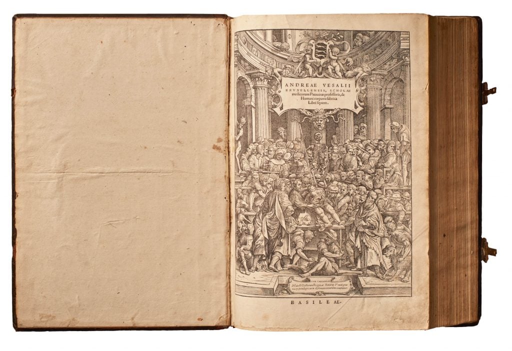 An Andreas Vesalius book open to a frontispiece showing an etching of an anatomy class