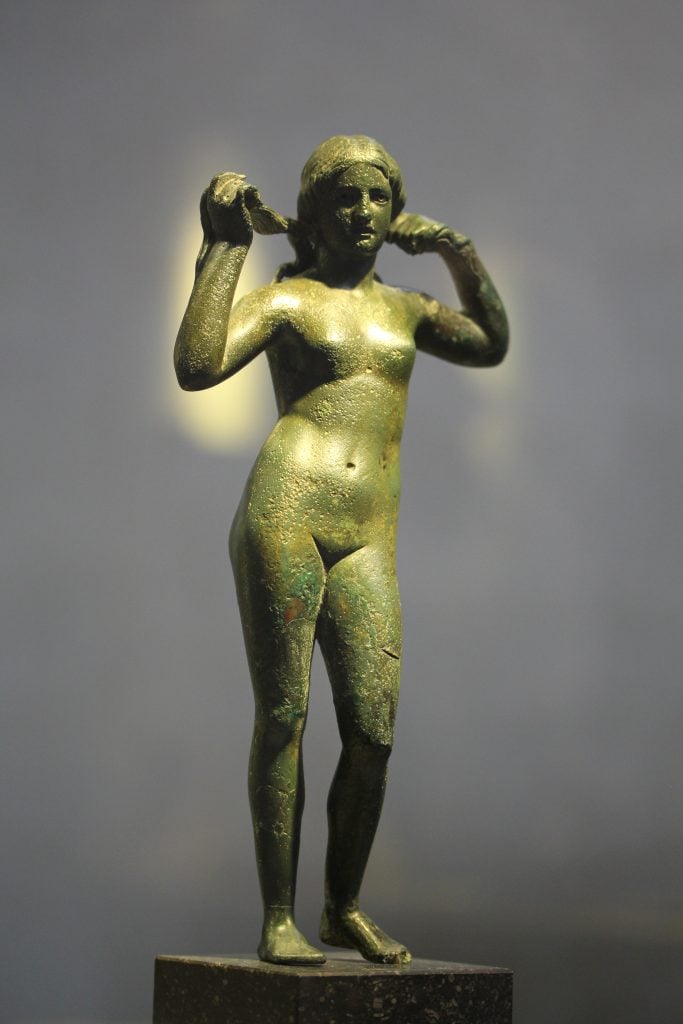 bronze statue of a nude woman raising her hands and wringing out her hari