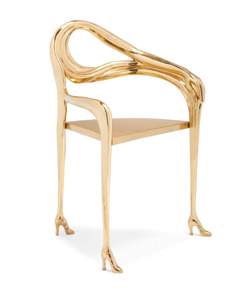 A chrome gold three legged chair where the feet resemble small women's high heels and the back is a curved human arm, included in the Art and Design sale at John Moran.
