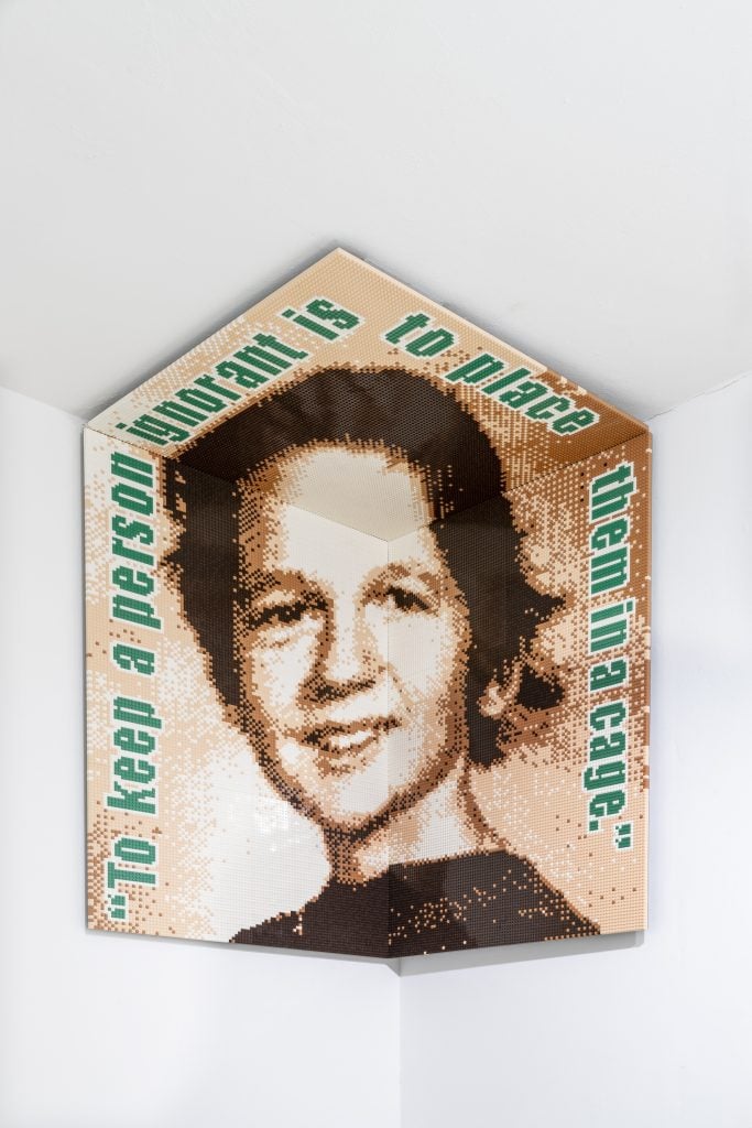 Artwork by Ai Weiwei that has vintage headshot portrait of a woman folded into the ceiling corner with digitized text in teal around the circumference with the title of the work.