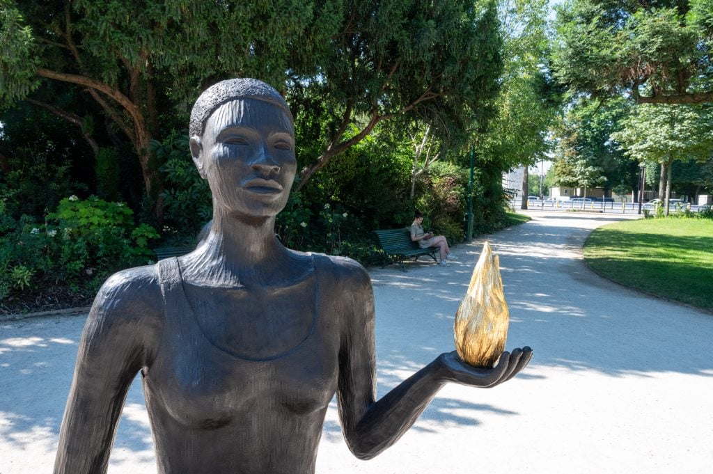 A bronze sculpture of a Black woman holding a golden flame