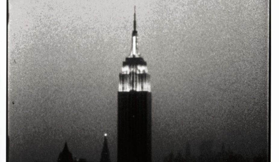 A black and white film still of the Empire State Building illuminated at night from an Andy Warhol film.
