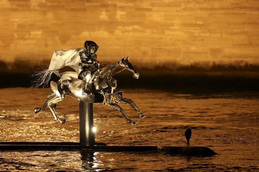 An armored horsewoman, wearing the flag of the International Olympic Committee (IOC), is seen on a metal horse sculpture designed by Atelier blam. She is riding on the River Seine during the opening ceremony of the Olympic Games Paris 2024 on July 26, 2024 in Paris, France. 