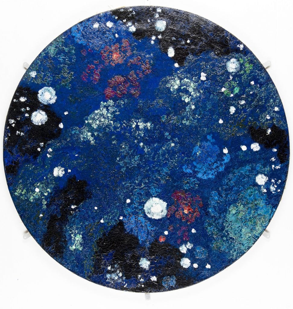 A circular canvas with a deep blue background with red and white paint splatters