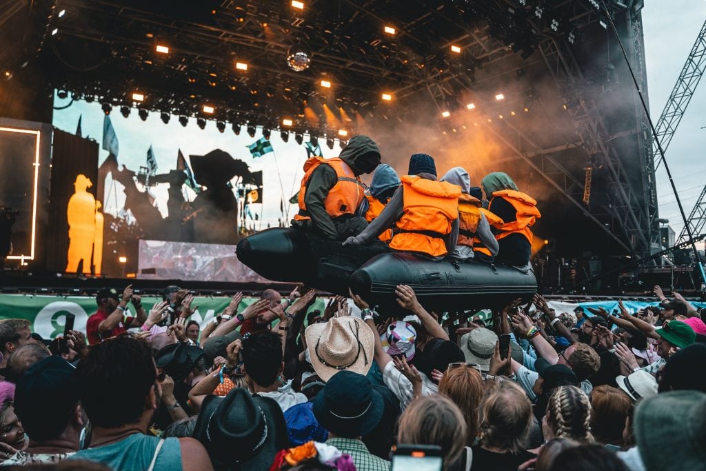 A small inflatable boat with several dummy figures aboard surfs the crowd at a concert