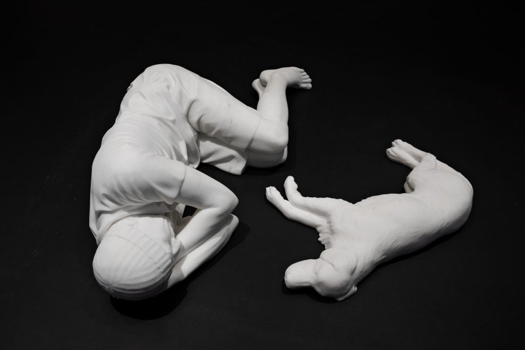white models of the figure of a boy and a dog are lying down side by side as though asleep