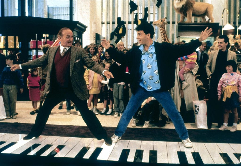 Actors Robert Loggia and Tom Hanks dancing on top of a large keyboard in front of a crowd of children.