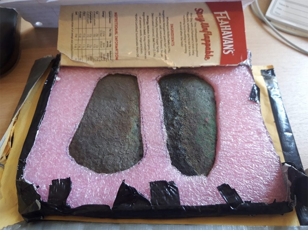 Two ancient axe-heads packaged in pink foam in a cardboard box.