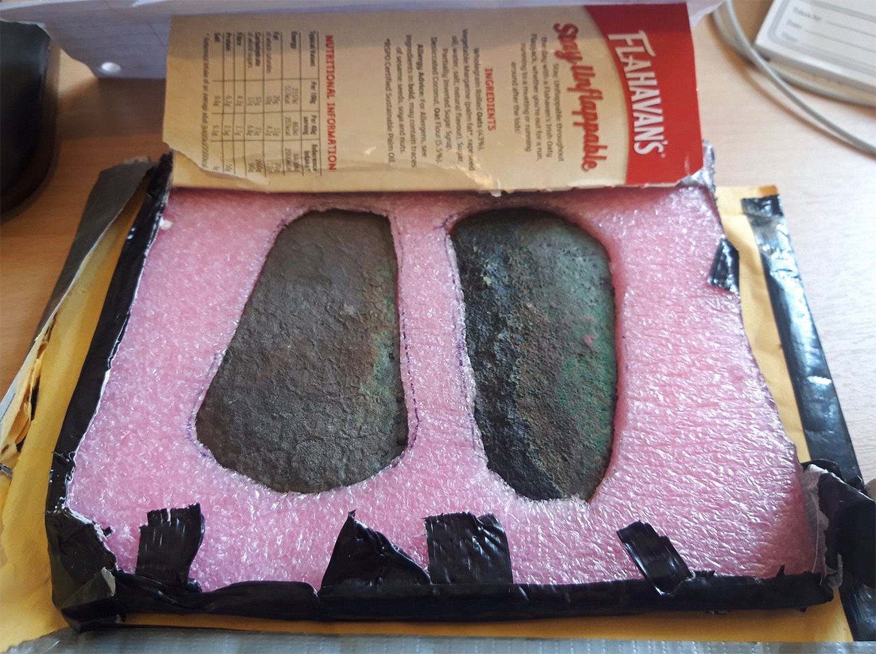 Two ancient axe-heads packaged in pink foam in a cardboard box.