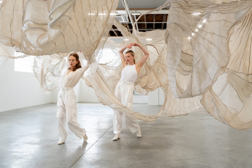 Sara Mearns and Jodi Melnick side by side with the former looking at the camera in poses from a dance performance inside a textile installation at Carvahlo Park.