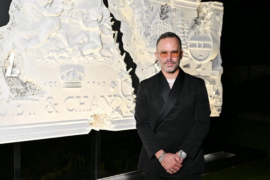 Sculptor Daniel Arsham standing in front of a cracked white frieze