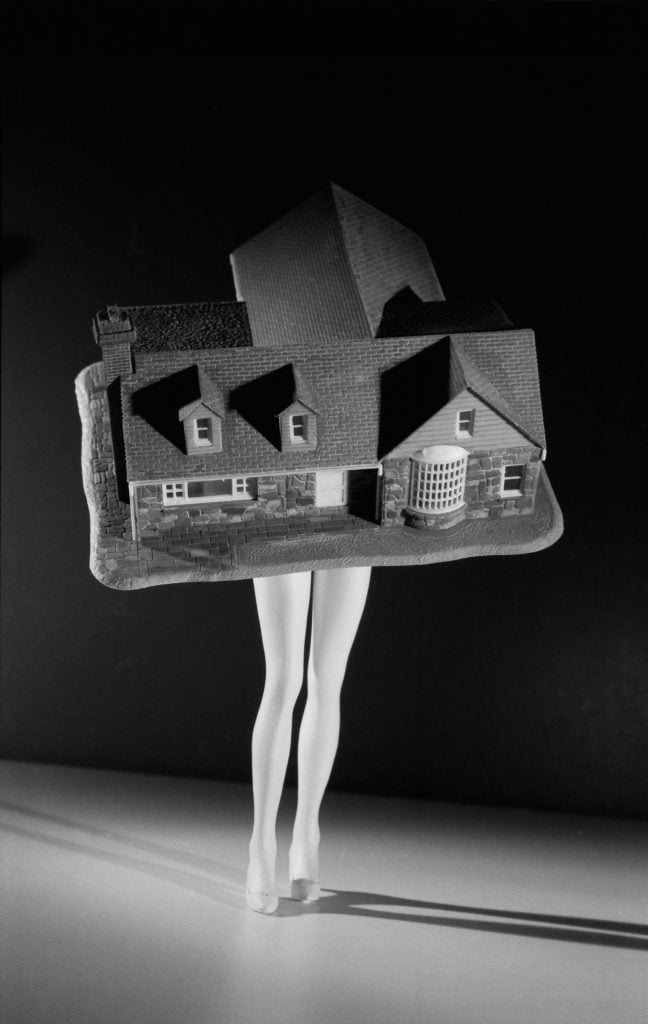 A black and white photo of a model house on top of a pair of mannequin legs