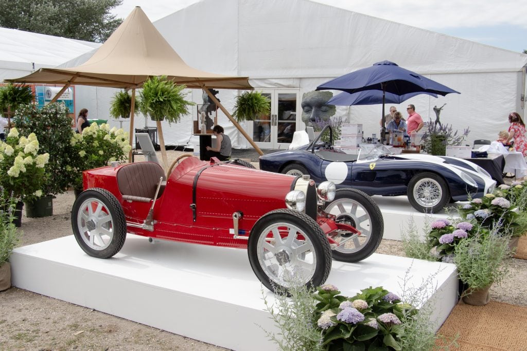 Two vintage cars on pedestals outside the tent holding the Hamptons Fine Art Fair 2024.