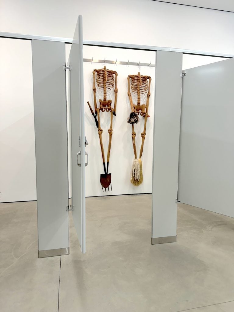 Two wooden sculptures of skeletons huge in a bathroom stall in an art gallery