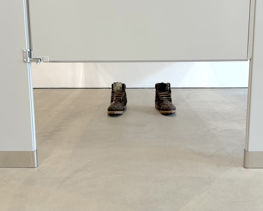 A sculpture of two booted feet seen under the door of a bathroom stall