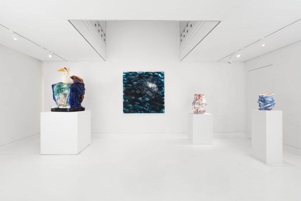 Installation view of group show Nature's Reflections, a white cube style gallery space with a square, dark painting on the wall and three sculptures on white pedestals.