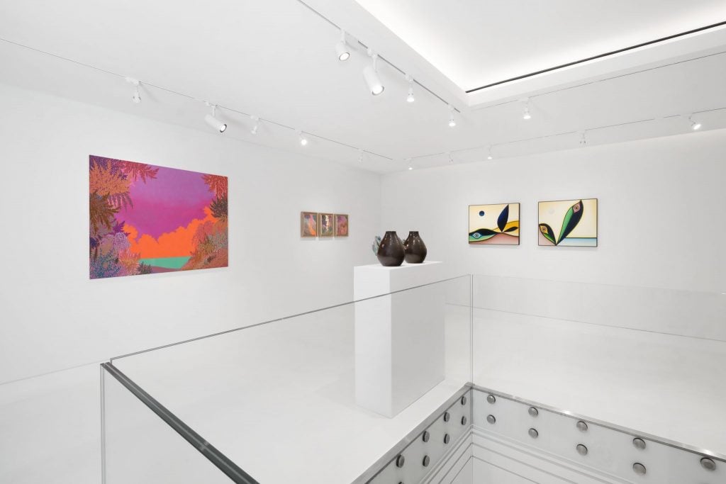 Installation view inside a gallery's second floor space with glass banister with four paintings and two small sculptures on pedestals.