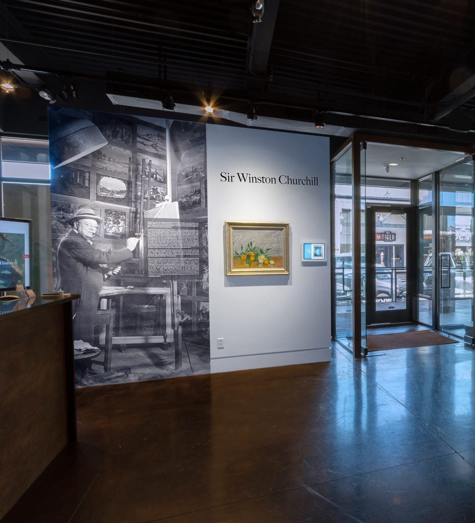 Installation view of entryway to Winston Churchill exhibition at Heather James Fine Art, with a painting installed on the wall as well as oversized graphic vintage photo of the artist.